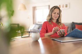 Woman using cell phone on dining table at home