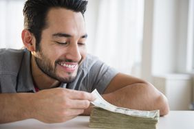 A man grins as a large stack of currency laying on a table