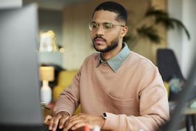 person in peach sweater wearing glasses looking at computer