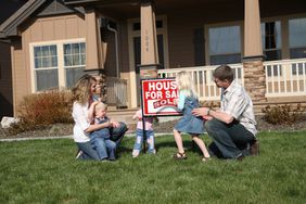 Parents and three young children placing a sold sign in front of their home