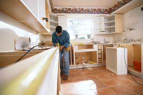 Man measuring counter amid kitchen that's being renovated