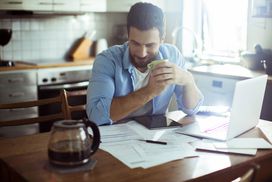 Man consulting financial paperwork with coffee at kitchen table