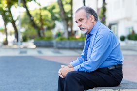 Man in tie sits on outdoor bench looking dejected