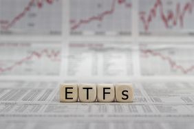 Block letters spelling ETFs on top of stock market reports and graphs.