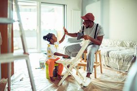 Close up of a father and daughter painting a chair in a house under construction