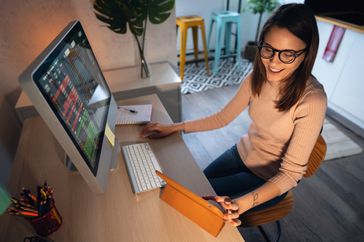 Bespectacled woman trading on her computer and laptop at home