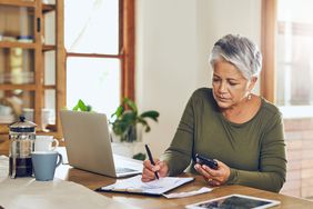 Woman with gray hair sits at a desk to work on her household budget