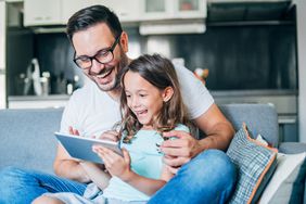 Young father and his cute small daughter having fun with digital tablet on couch.