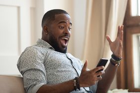 A surprised man looks at his phone in happiness and excitement