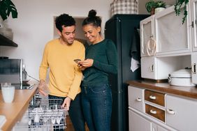 A couple looks at their mortgage balance on a phone while standing in a kitchen