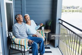 Laughing older couple seated on the porch of their home, overlooking waterway