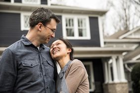 A man and woman hug each other in front of the new home they have just purchased.