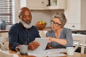 Senior couple using a digital tablet while going over bills and paperwork together at home