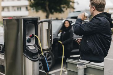 Person drinking coffee while waiting for car to charge at a charging station