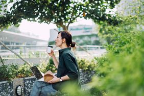 Woman working on a laptop and enjoying coffee sitting in a park