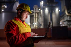 A young engineer with a laptop enters air data at an oil refinery