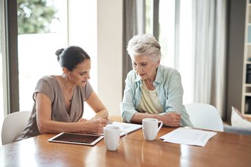 A parent and adult child sit at a kitchen table and review documents.