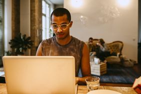 A person wearing glasses and a tank top looks at a laptop while sitting at a table