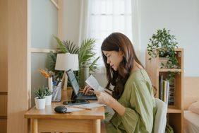 Asian woman holding various expense bills and entering them into computer 