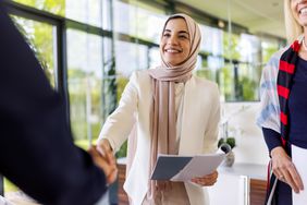 Woman in hijab holding papers and shaking hands with colleague