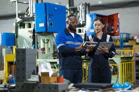 Two people hold tablets as they work in a manufacturing factory.
