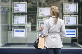 Woman looking at homes for sale ads placed in real estate window
