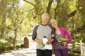 Mature couple with yoga exercise equipment walking in park
