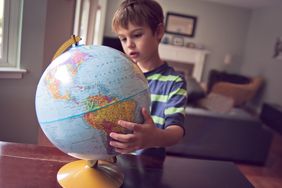 A child holds a globe at home, with North and South America facing the camera