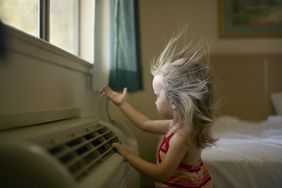 Toddler uses her hand to play with the air coming from a room air conditioner as it blows the hair away from her face