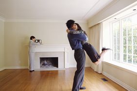 Couple embracing in new home, realtor in background