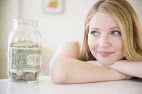 Woman smiling at the start of her savings of coins and bills in a jar