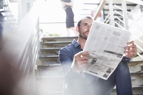 Man reading the newspaper while sitting on stairs