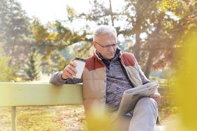 Older man reading paper with coffee on a bench