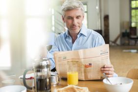 Older man having breakfast and reading the paper