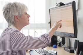 Senior woman at desk pointing to stock information on a monitor