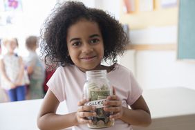 young girl holding a clear glass jar of money with a label showing the word "college"