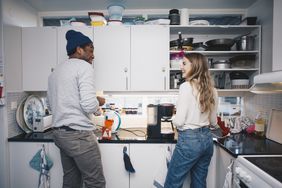 Two roommates stand in their kitchen, chatting over coffee