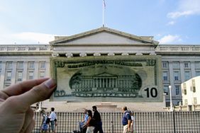 Hand holding up a $10 bill in front of the U.S. Treasury