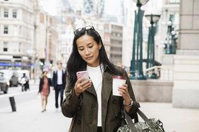 Businesswoman looks at smart phone while walking in city