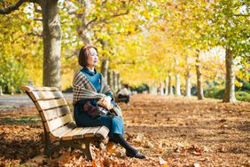 Older woman on a fixed annuity enjoying the fall weather on a park bench.
