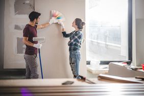 Couple choosing a paint color by holding up swatches to a wall