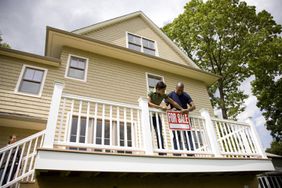 Two men hanging a "For Sale" sign on the deck of a "Coming Soon" house