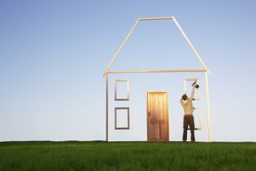 Man constructing a wooden image of a house against a blue sky
