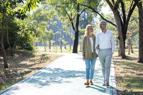 Senior couple walks arm in arm though sunny park
