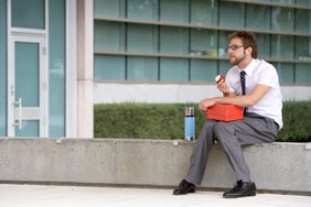 Man eating lunch on a ledge by an office building