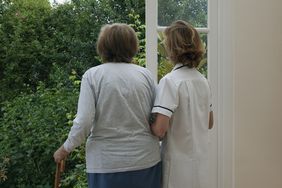 A nurse supporting an elderly woman as she stands at an open door