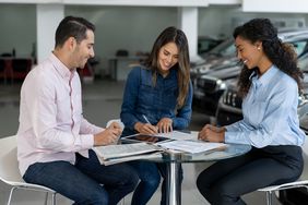 Couple buying a car from a saleswoman at a car dealership and signing a contract