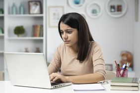 Young woman types on laptop in home office