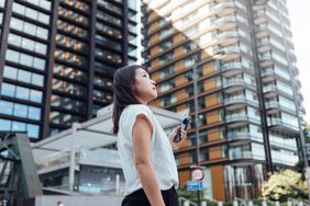 Woman with phone in hand looking at high-rise building 