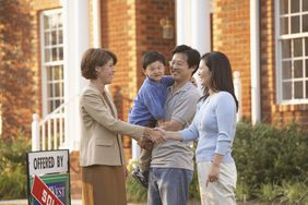 Family shaking hands with a real estate agent next to house
